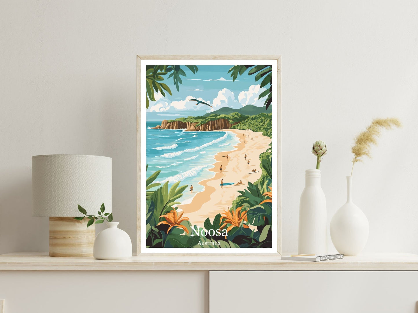 Framed artwork of a tropical beach scene with 'Noosa' on a shelf.